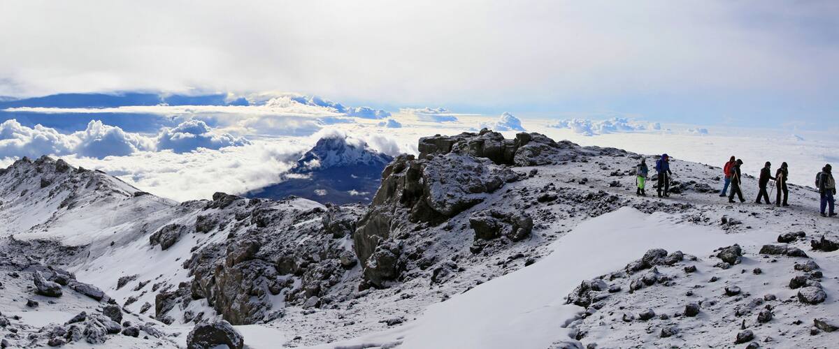 A snowy mountain peak with rocky terrain and a group of hikers.