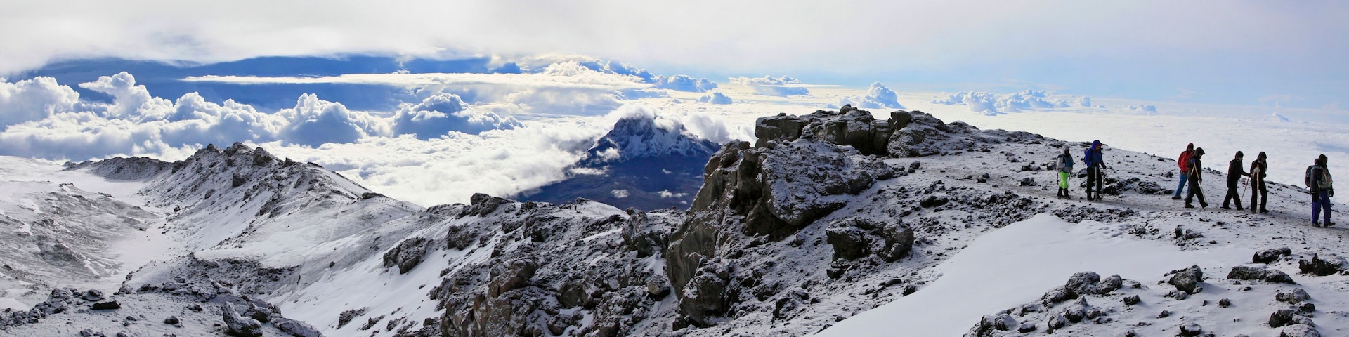A snowy mountain peak with rocky terrain and a group of hikers.