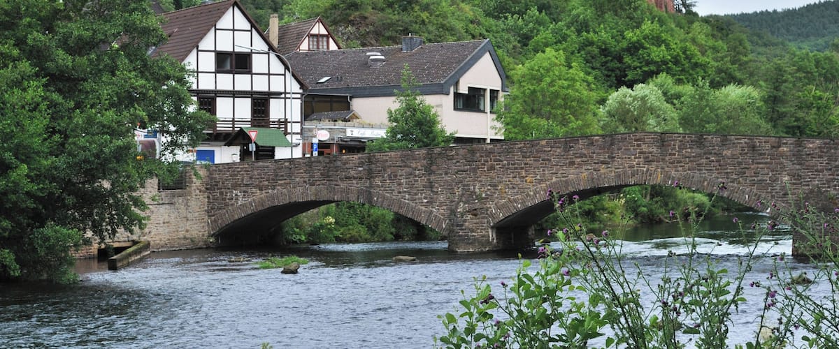 Castle Hengebach in Heimbach in the German Federal State North Rhine-Westphalia. In the front is seen the river Rur with a bridge.