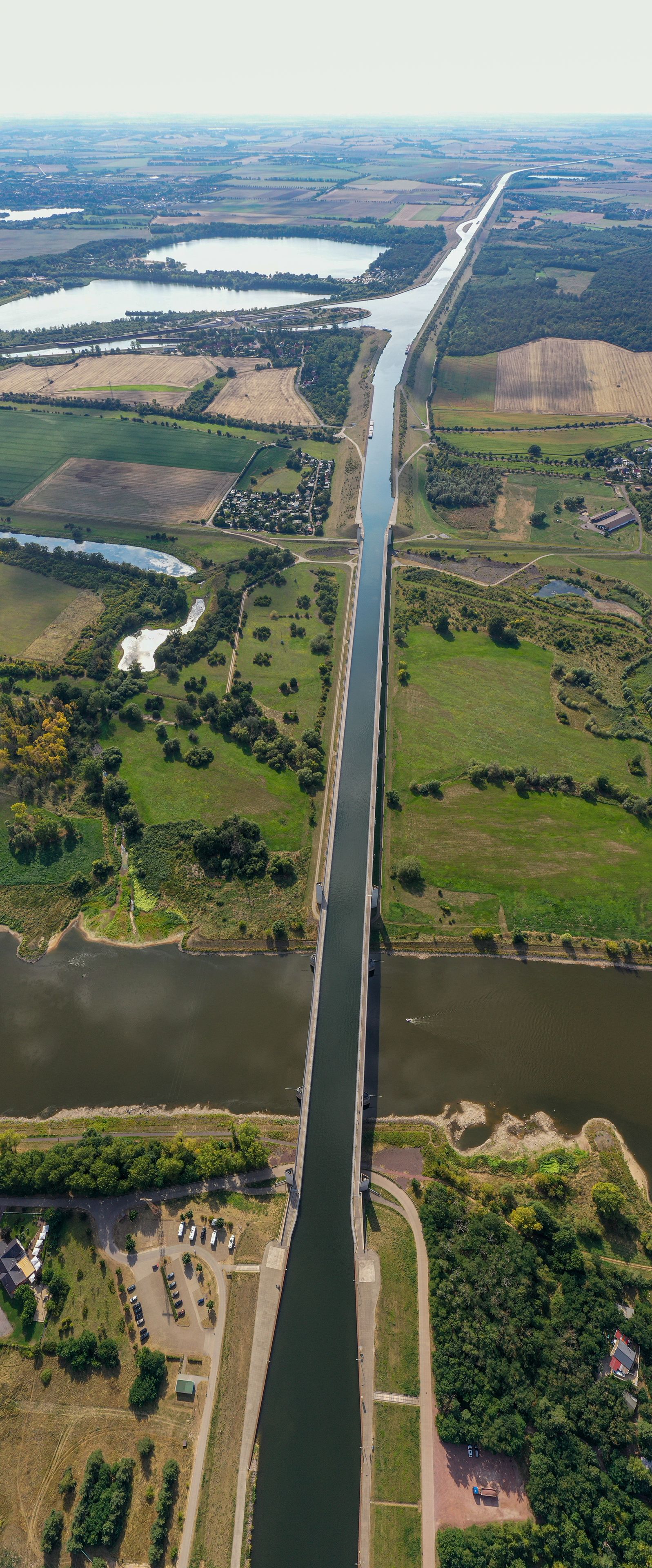 Een rivier met een brug, omringd door velden en een klein stadje.