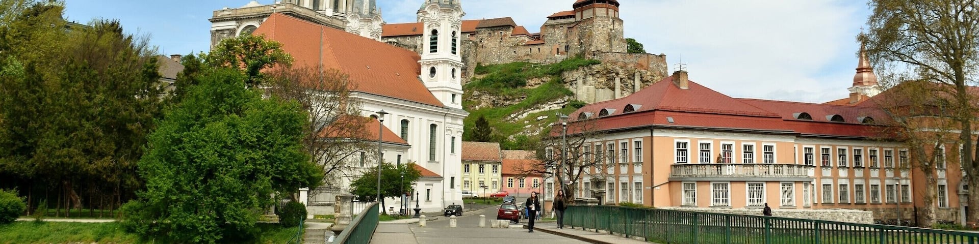 A historic town with a prominent church, a castle on a hill, and a green bridge.