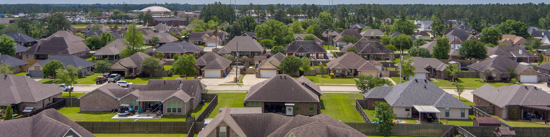 A suburban neighborhood with houses, a large building in the distance, and a cloudy sky.