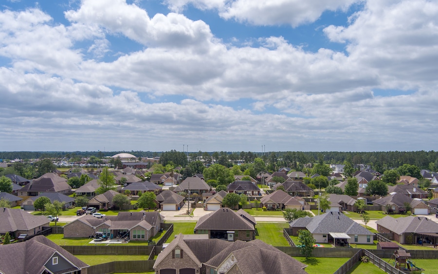 A suburban neighborhood with houses, a large building in the distance, and a cloudy sky.