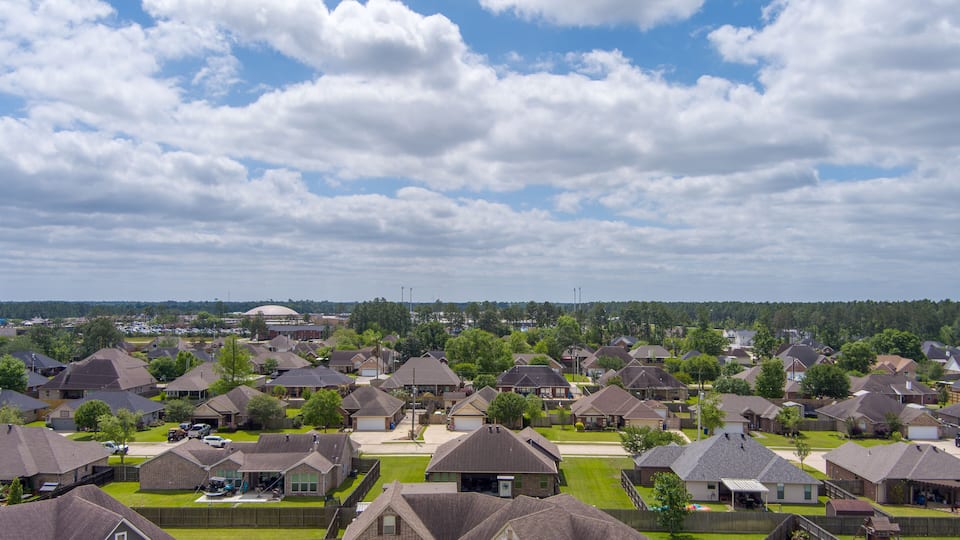 A suburban neighborhood with houses, a large building in the distance, and a cloudy sky.