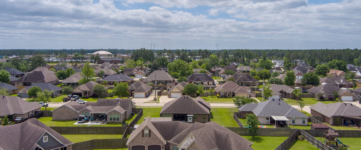 A suburban neighborhood with houses, a large building in the distance, and a cloudy sky.