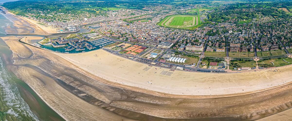 An aerial view of a coastal city with a marina, sandy beaches, and a large green sports field.