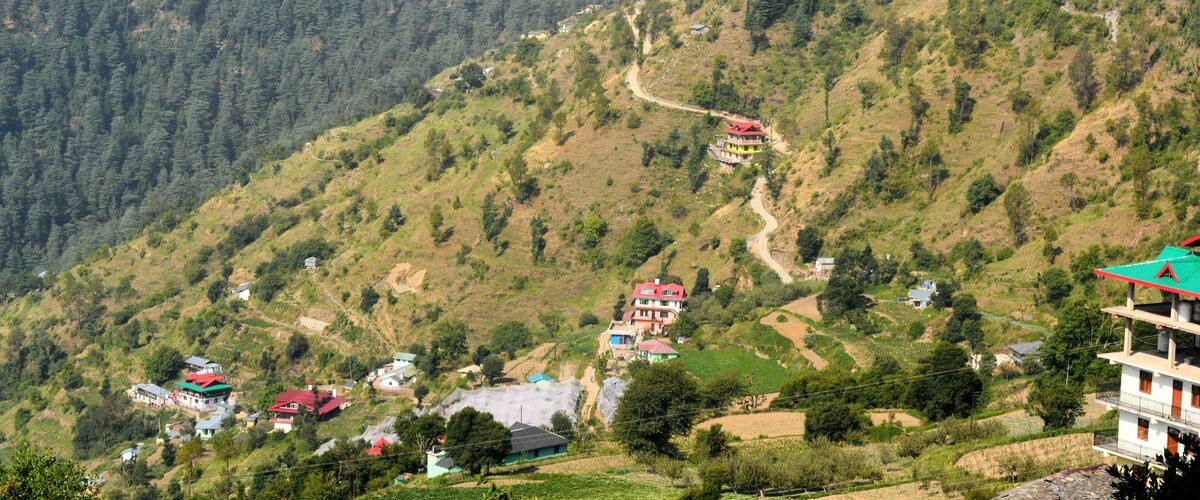 A mountainous landscape with terraced fields, houses with red roofs, and dense forested hills.