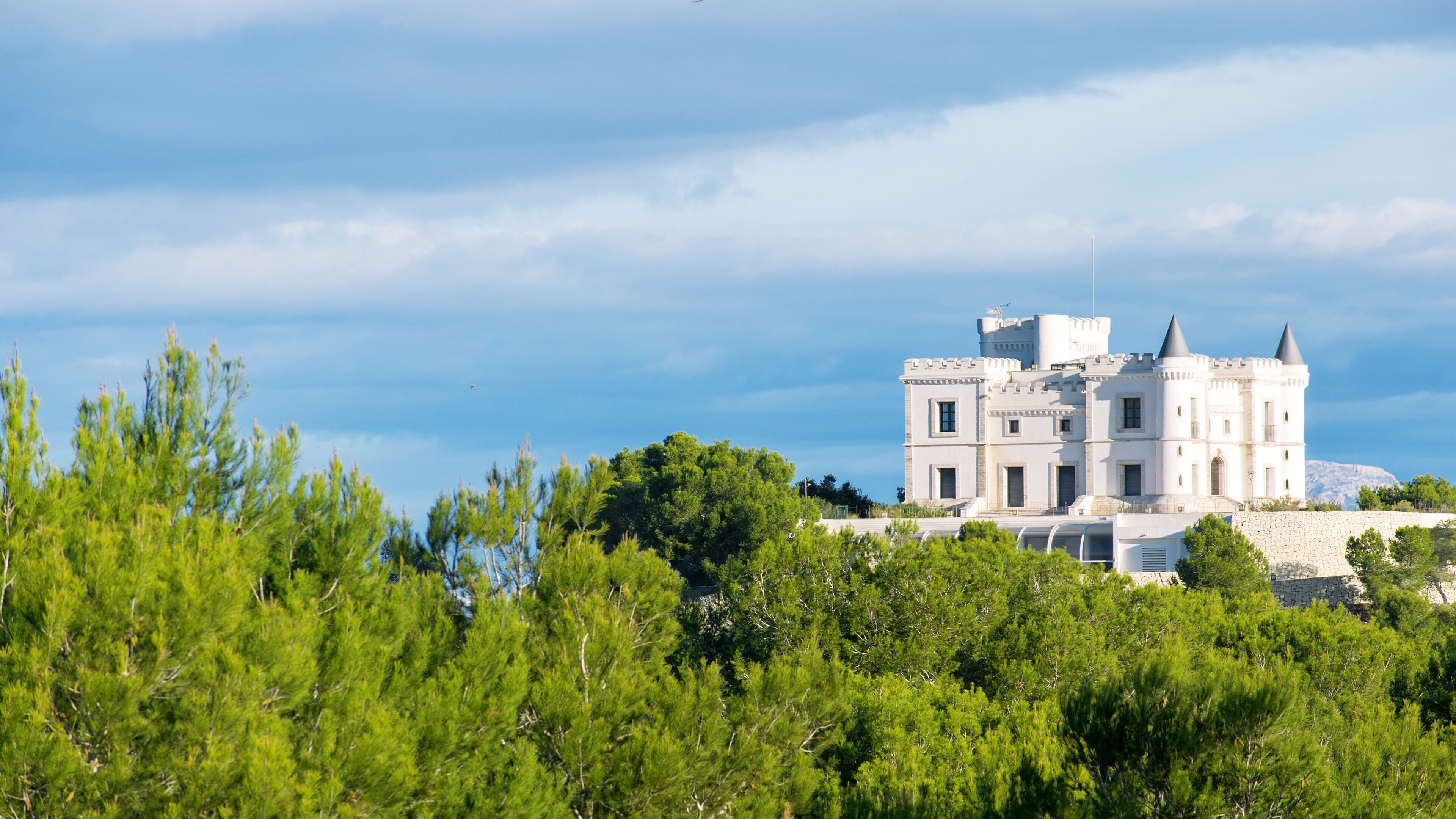 A white castle-like building with two towers, surrounded by green trees and a clear sky.