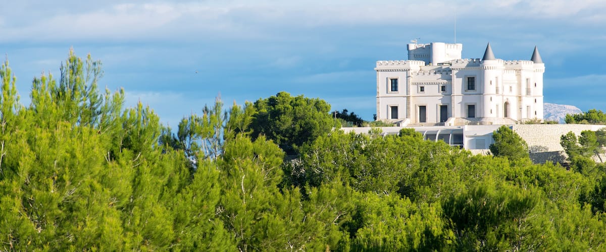 A white castle-like building with two towers, surrounded by green trees and a clear sky.