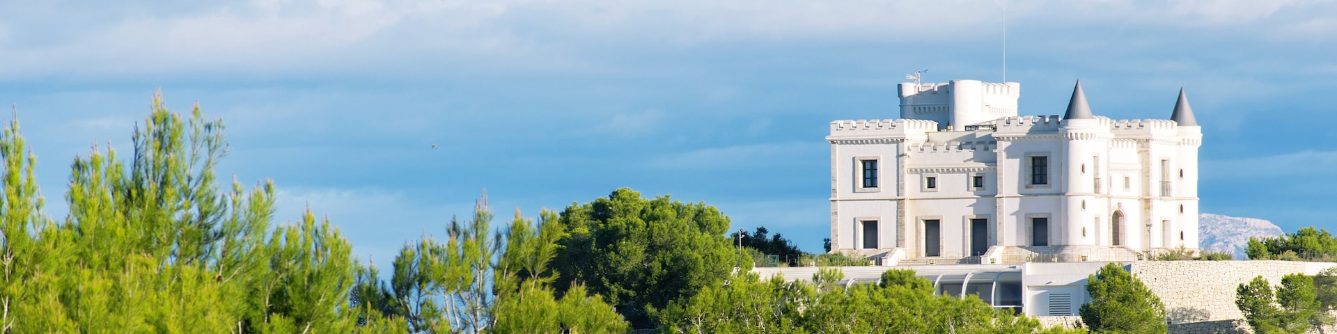 A white castle-like building with two towers, surrounded by green trees and a clear sky.