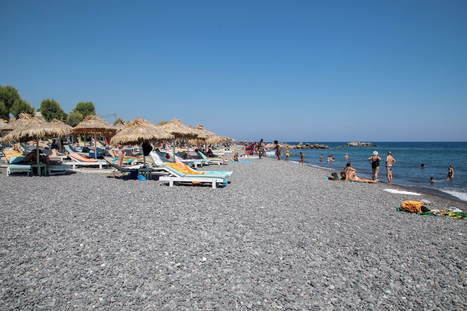 A pebbled beach with sun loungers and thatched umbrellas.