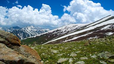 A mountain landscape with snow-covered slopes, rocky terrain, and a clear blue sky.