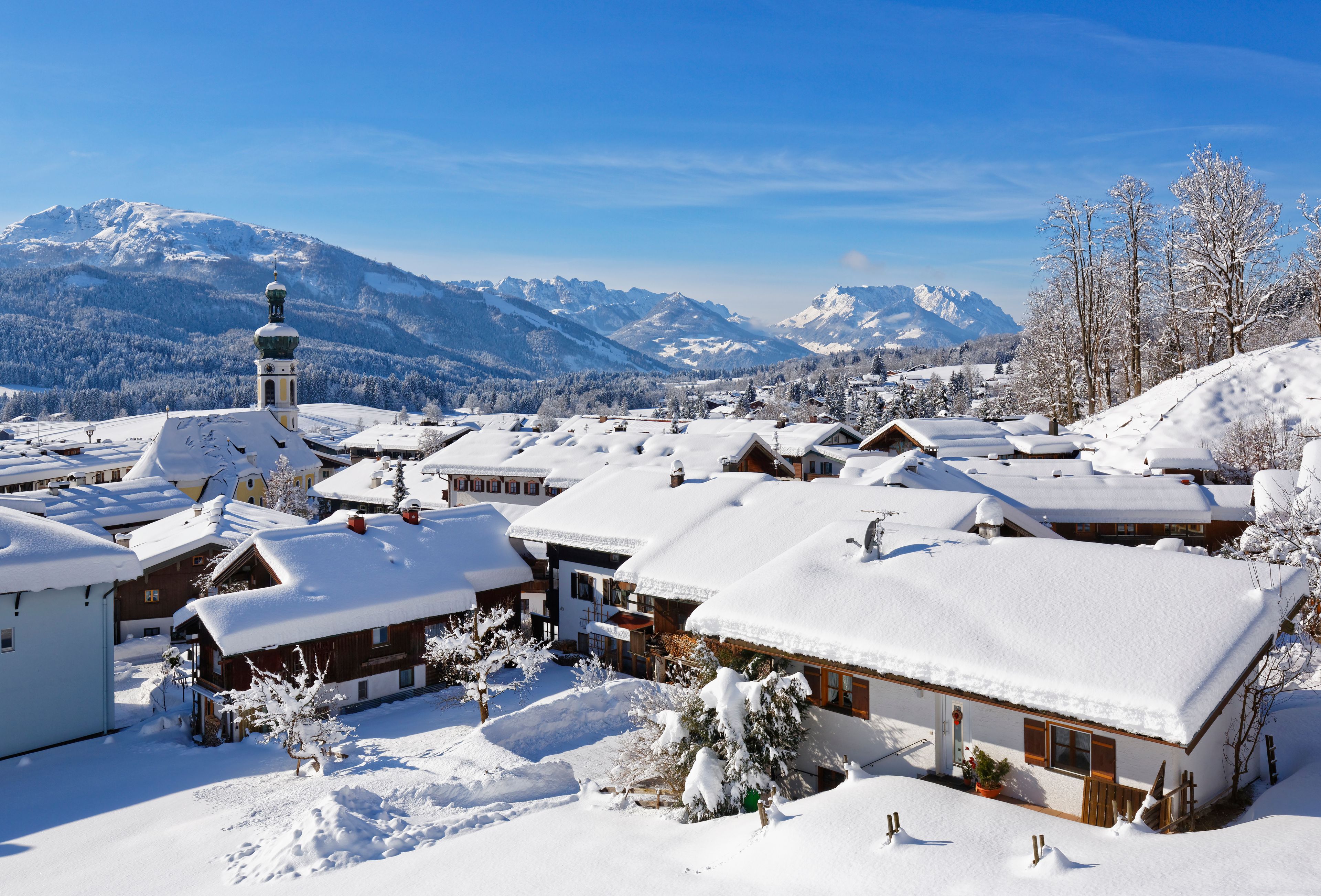 A snow-covered village with traditional houses, a church, and mountains in the background.