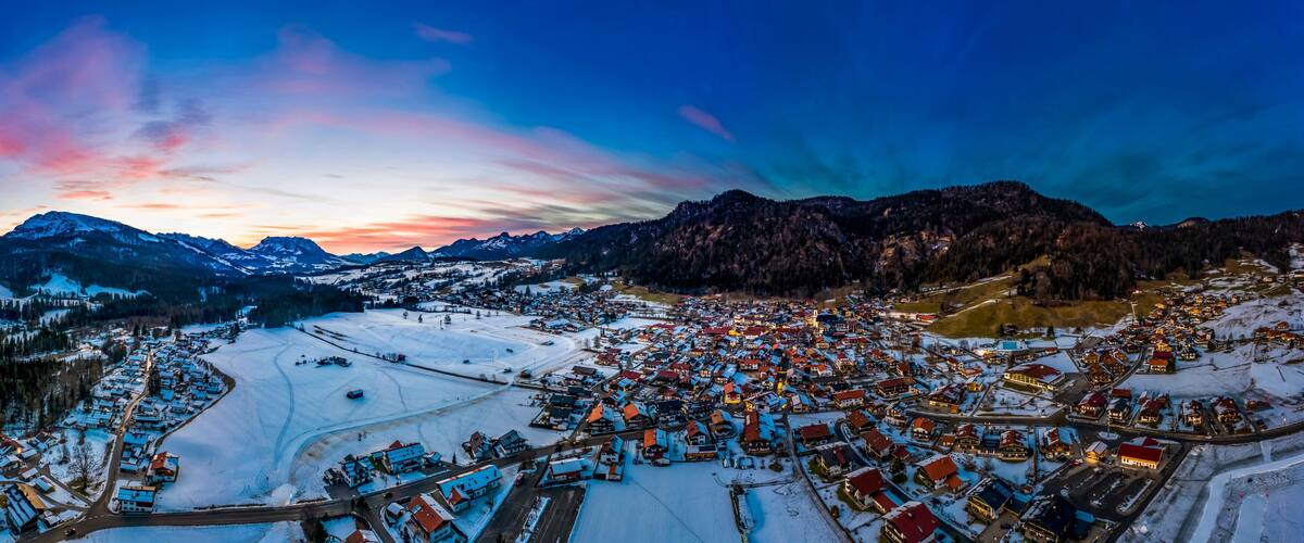 A snow-covered town with mountains in the background and a colorful sunset sky.