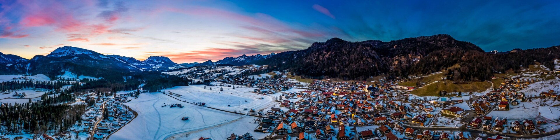 A snow-covered town with mountains in the background and a colorful sunset sky.