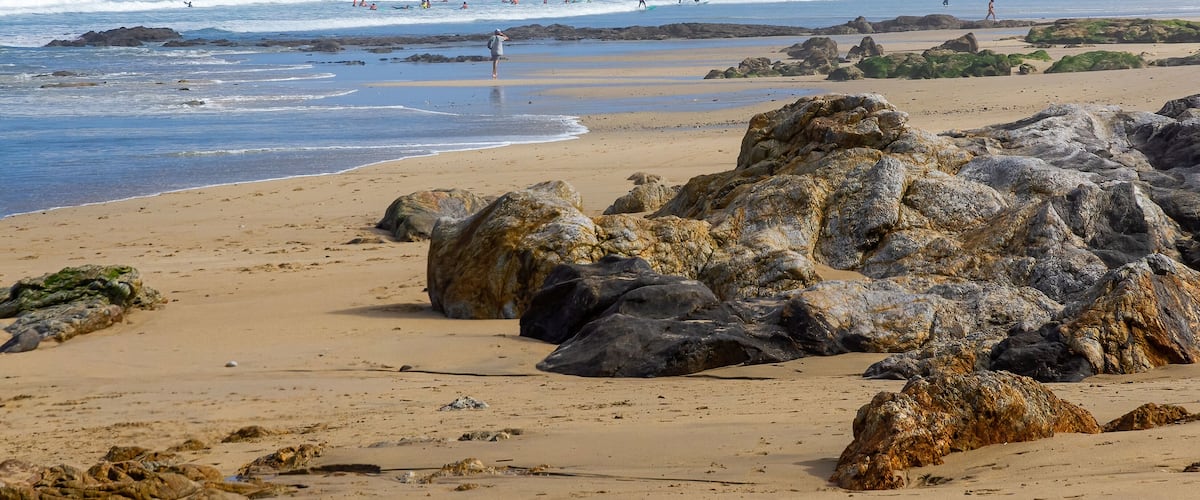 A rocky beach with waves crashing onto the shore and people surfing.