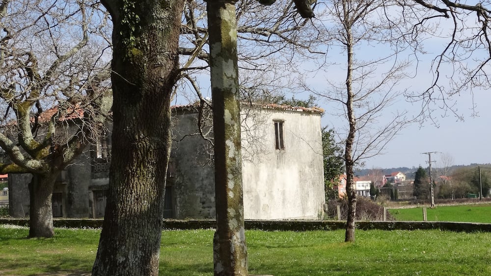 A stone cross in a grassy area with trees and a building in the background.