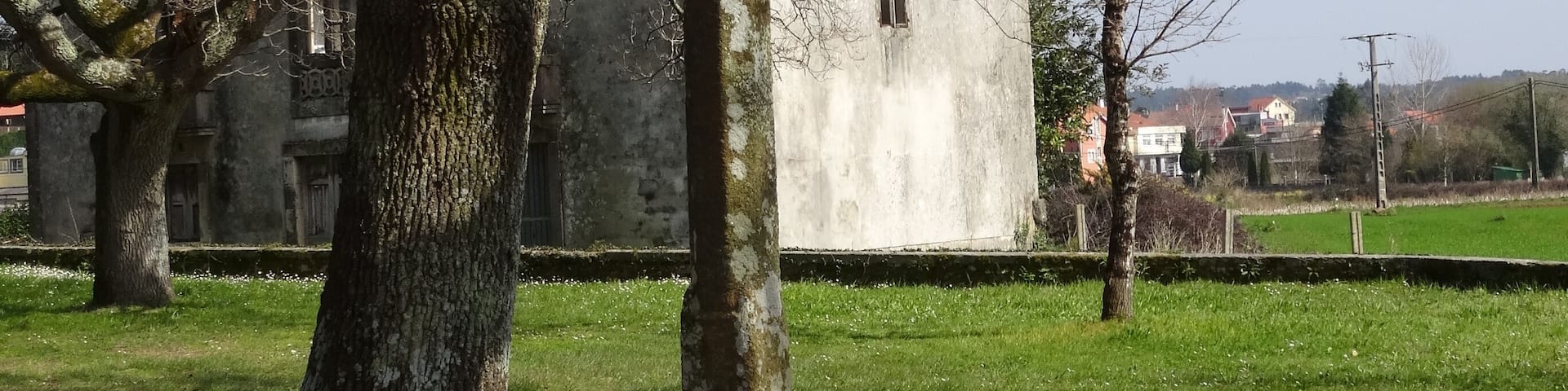 A stone cross in a grassy area with trees and a building in the background.