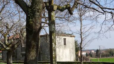 Una cruz de piedra en un área con césped, árboles y un edificio al fondo.