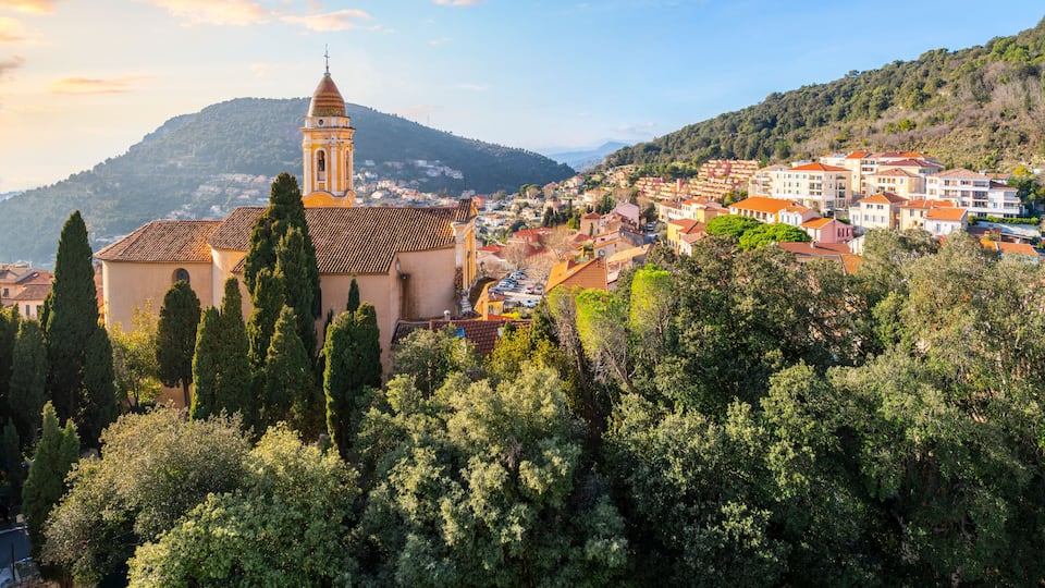A town with a prominent church, dense greenery, and a hill in the background.