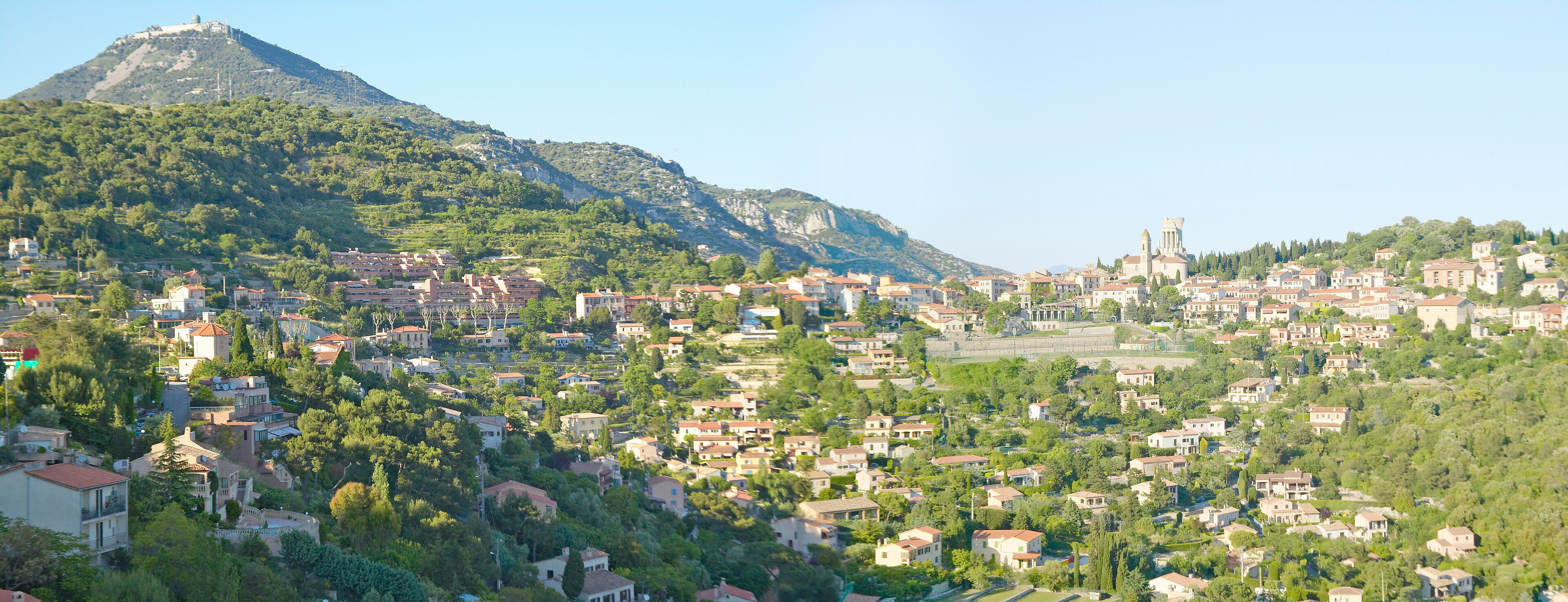 A town nestled in a valley with a prominent mountain in the background and a church with a bell tower.