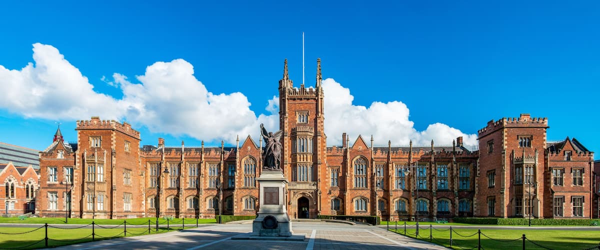 A large, historic brick building with a prominent tower, surrounded by well-maintained lawns and a clear blue sky.