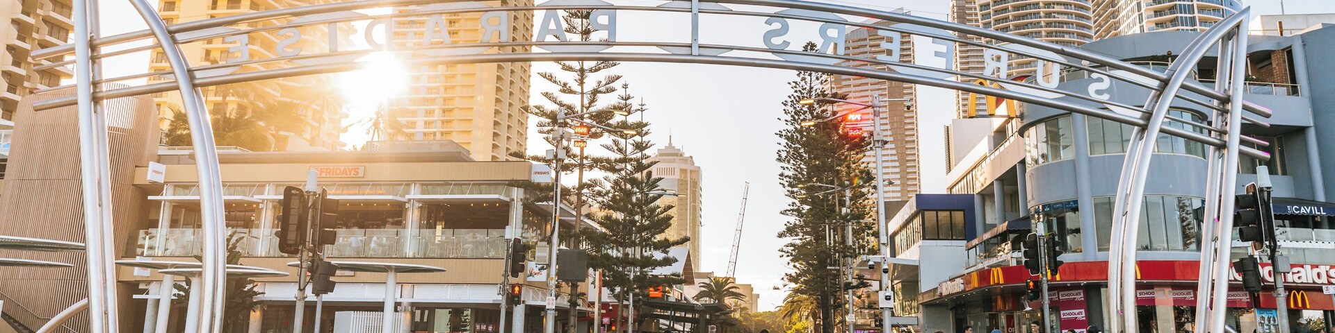 Rua movimentada em área urbana, com edifícios modernos, faixa de pedestres e céu claro.
