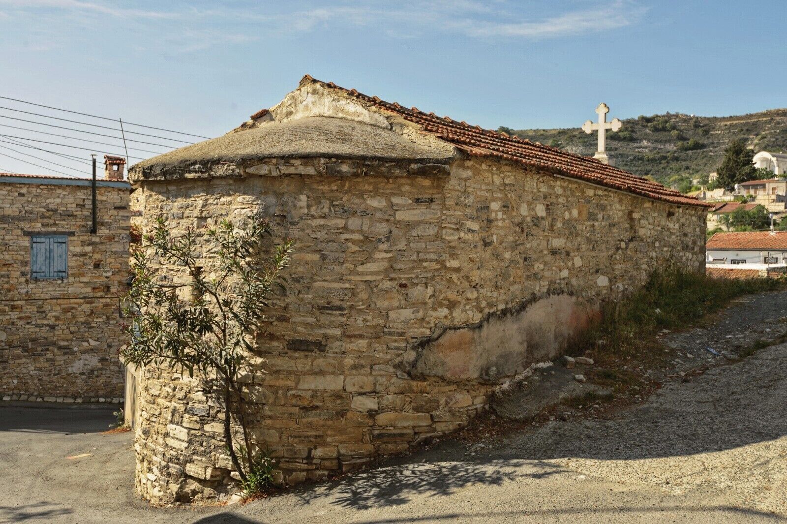 A stone building with a tiled roof, a cross, and a hill in the background.