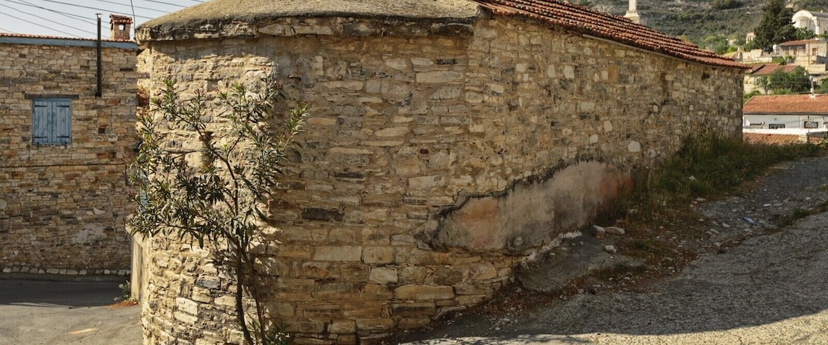 A stone building with a tiled roof, a cross, and a hill in the background.