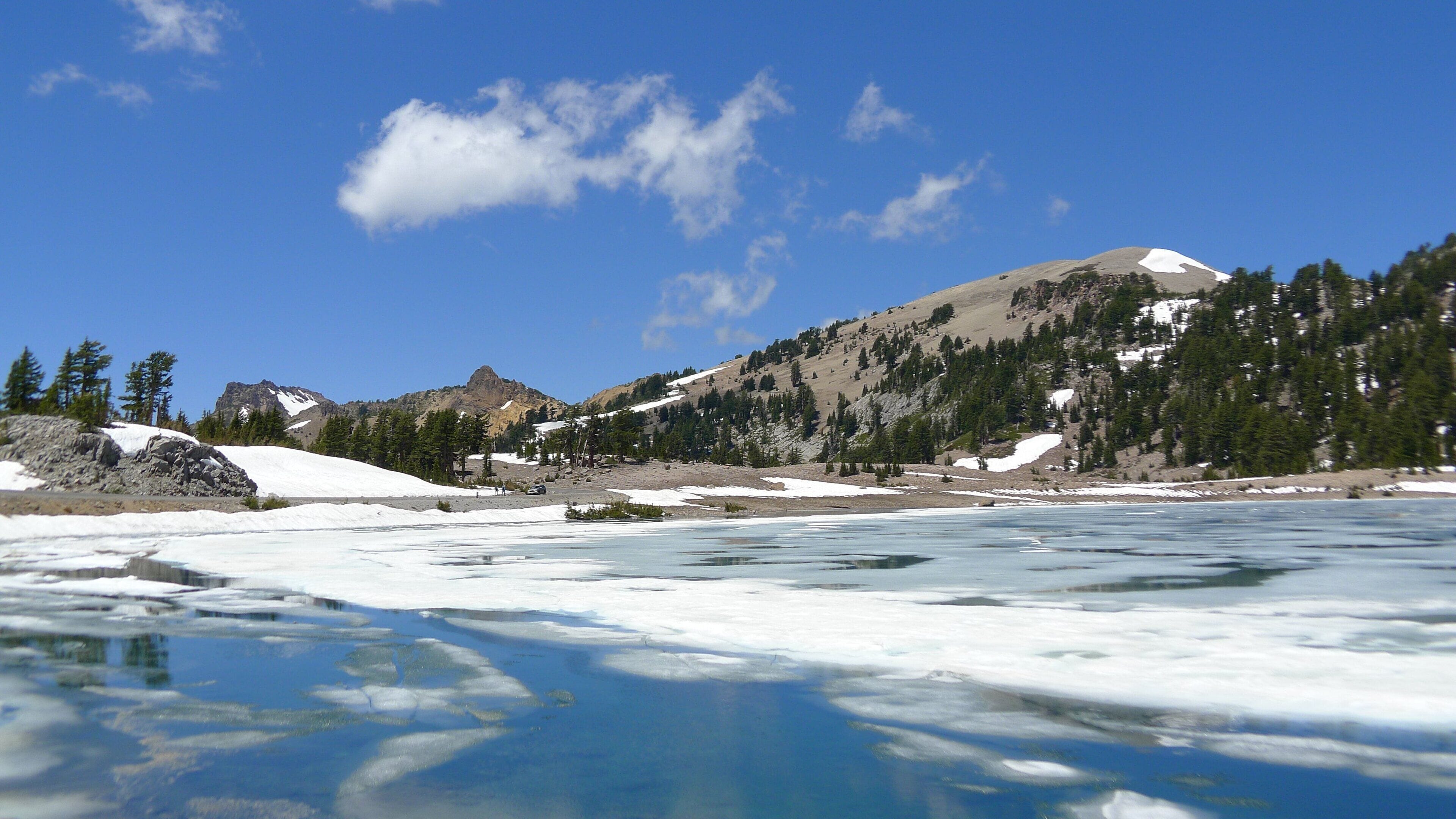 A frozen river with snow-covered mountains and trees in the background.