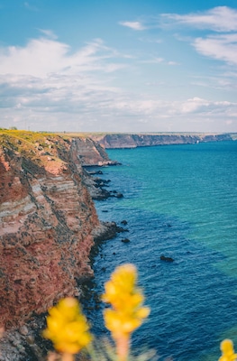A coastal landscape with cliffs, clear blue sea, and wind turbines in the distance.