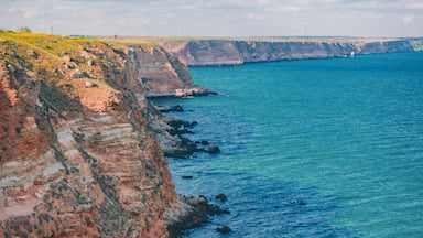 Un paisaje costero con acantilados, mar azul cristalino y aerogeneradores a lo lejos.