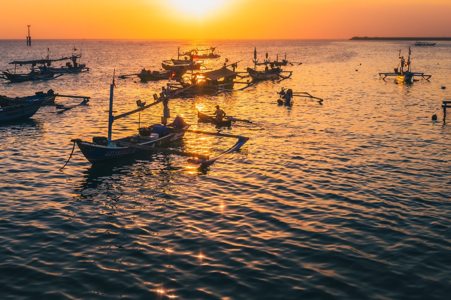 Un atardecer sobre un mar tranquilo con varias embarcaciones ancladas, reflejando los cálidos colores del cielo.