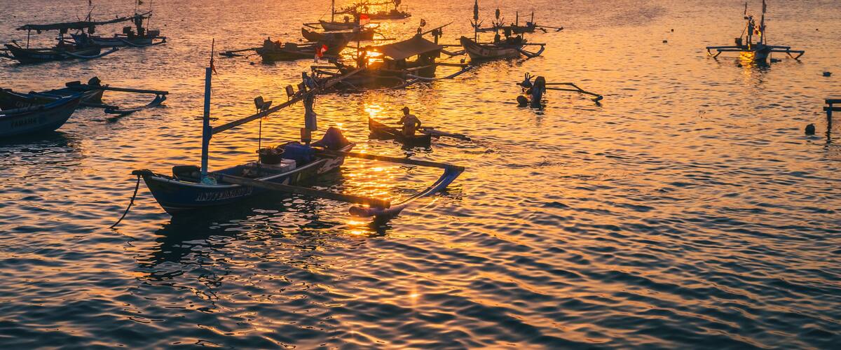 A sunset over a calm sea with several boats anchored, reflecting the warm colors of the sky.