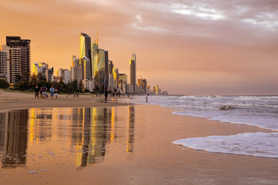 A beach with waves, a city skyline, and a sunset.