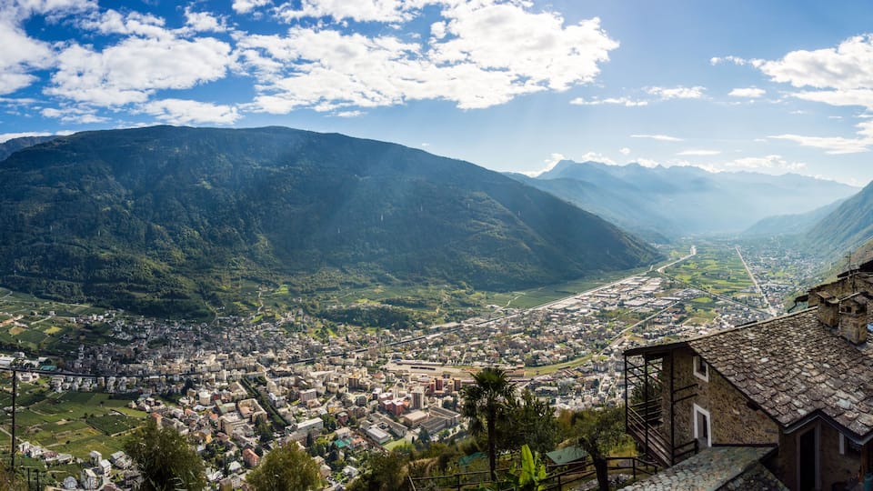 A mountainous landscape with a town nestled in a valley, surrounded by lush greenery and distant peaks.