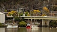 A bridge over a river with boats docked nearby and a rocky hillside in the background.