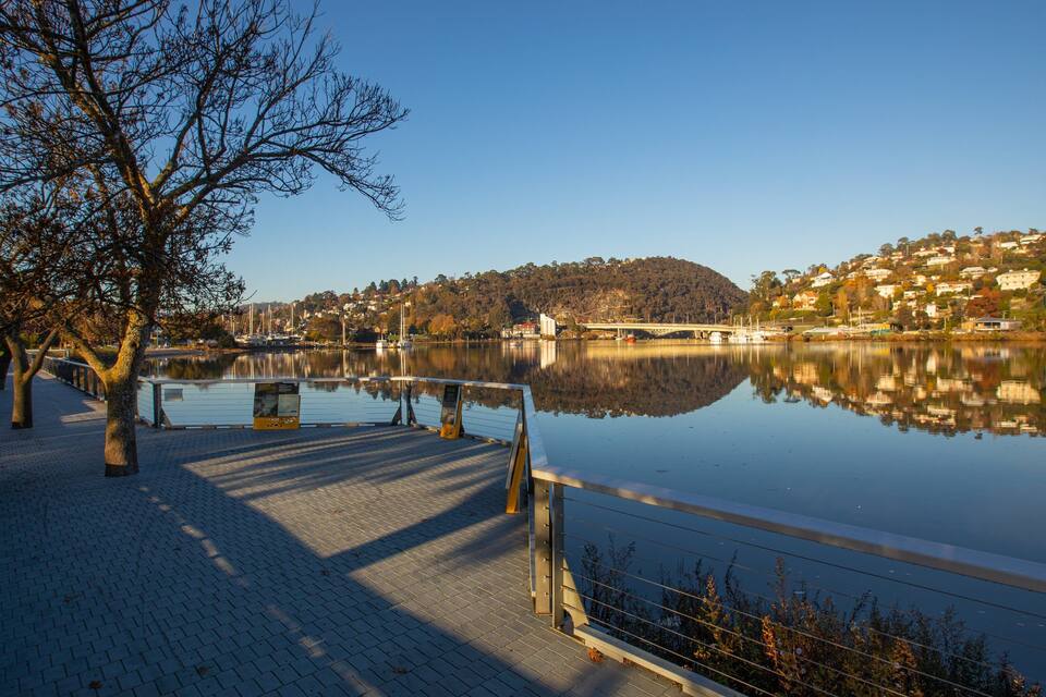 A calm lake with a dock, trees, and a hilly town in the background.