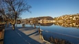 A calm lake with a dock, trees, and a hilly town in the background.