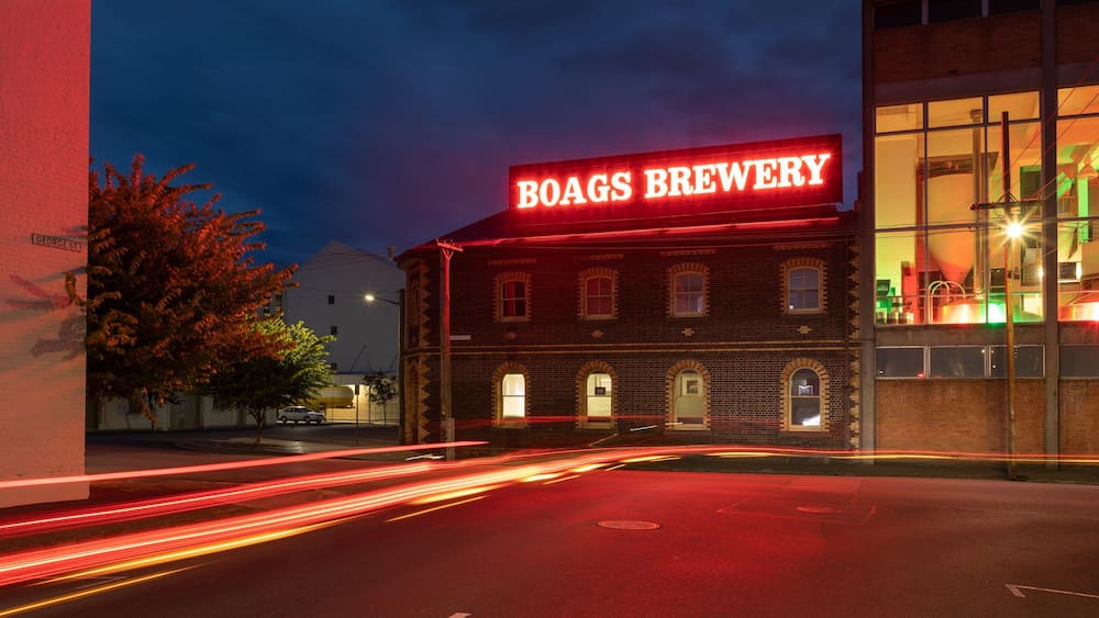 A building with a neon sign reading "BOAGS BREWERY" at night.