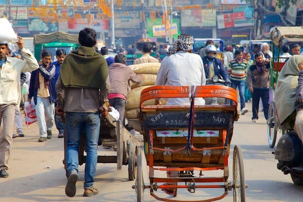Une rue animée où l’on voit des gens qui se promènent, un homme portant un grand sac sur la tête, et un chariot rempli de sacs étiquetés « SAFI ».