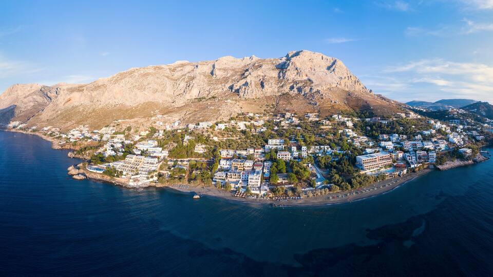 An aerial view of a coastal town with a prominent mountain, a beach, and a clear blue sea.