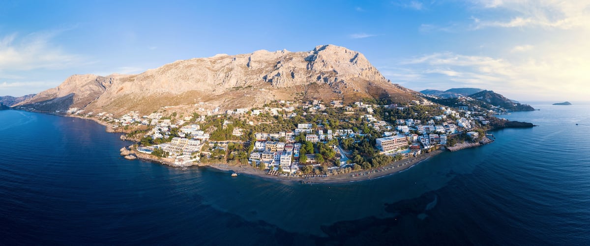 An aerial view of a coastal town with a prominent mountain, a beach, and a clear blue sea.