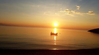 A boat on calm water during sunset with the sun low on the horizon.