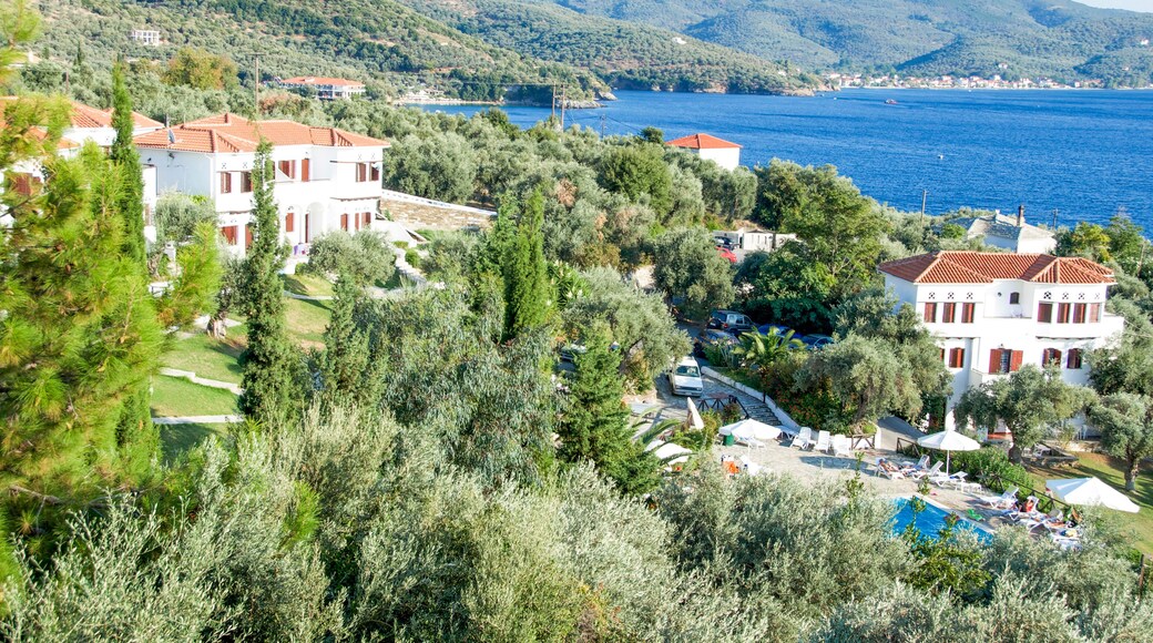 A coastal village with white buildings, a swimming pool, and a view of the sea and mountains.
