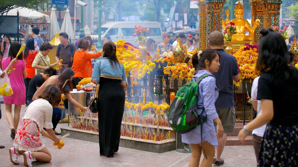 Una calle animada con gente realizando rituales, palitos de incienso y una estatua dorada.