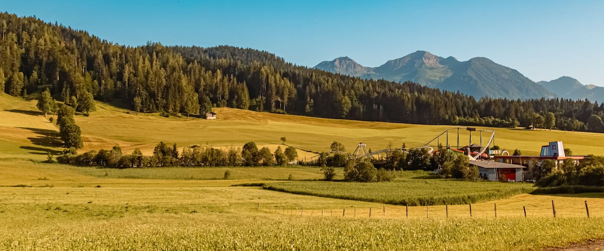 A rural landscape with a field, a small house, and a roller coaster in the background.