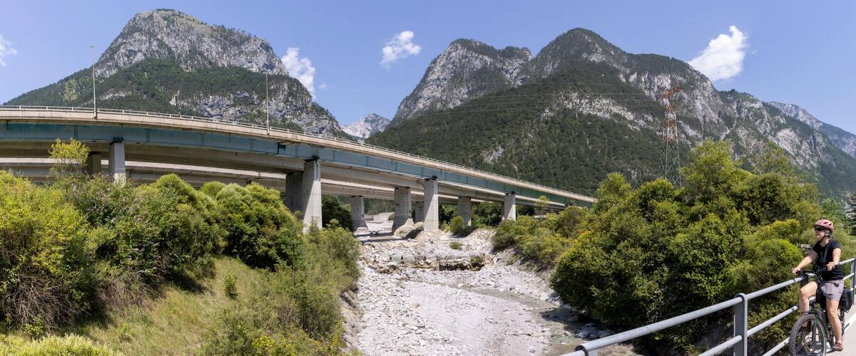 A mountain road with a bridge, rocky terrain, and dense greenery.