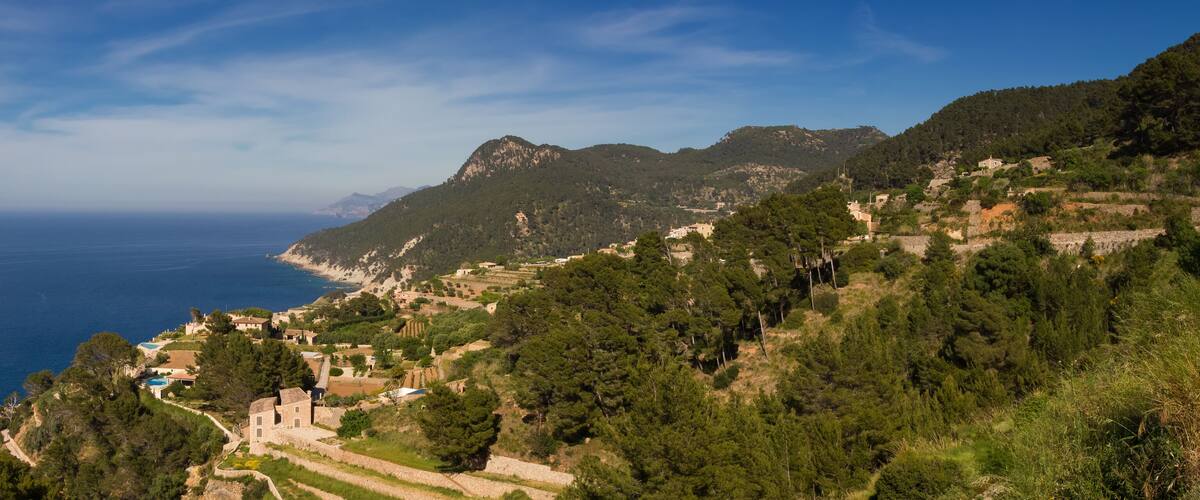 A coastal village with terraced fields, a stone church, and a view of the sea.