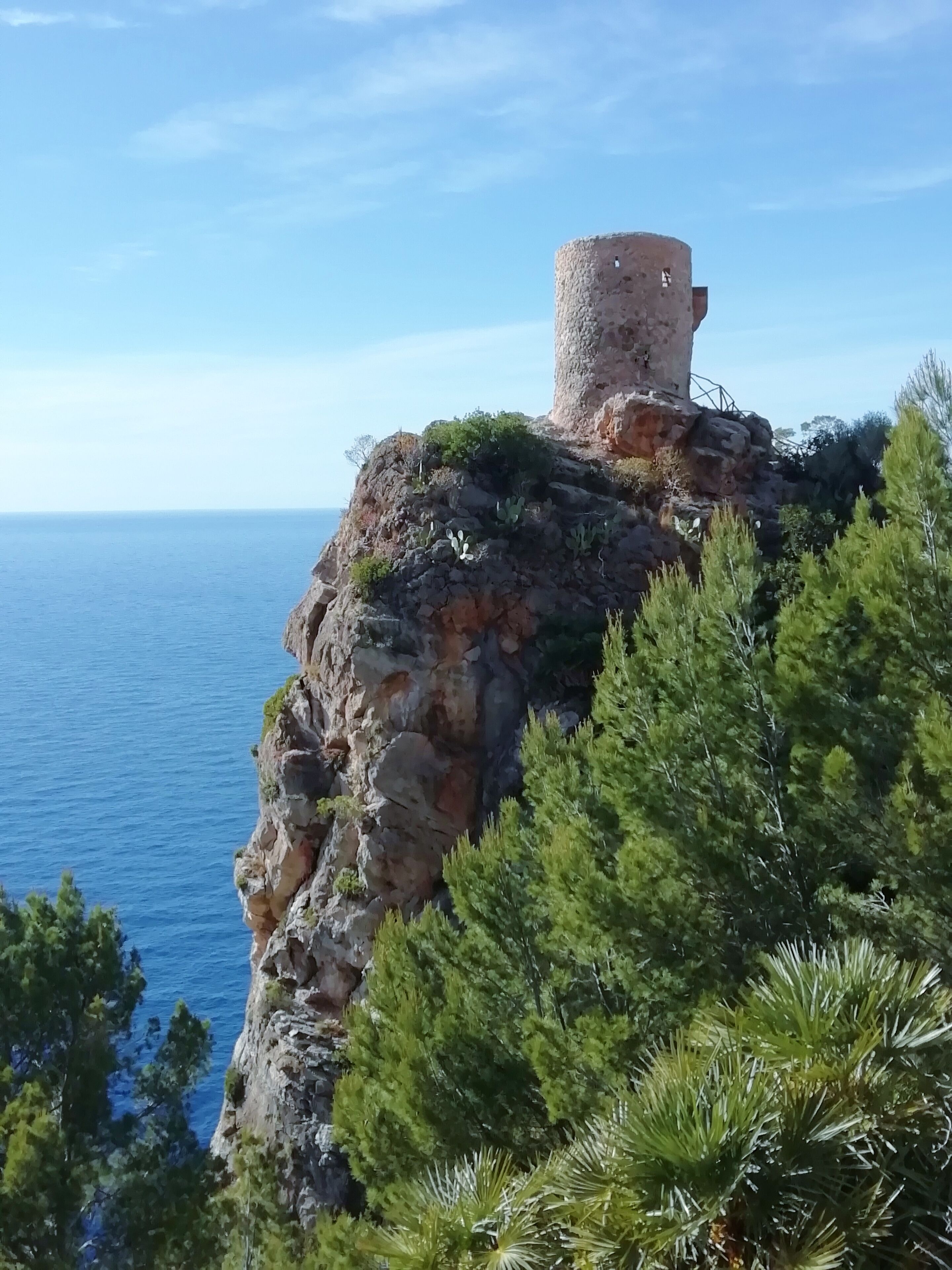 A coastal cliff with a tower and dense greenery.